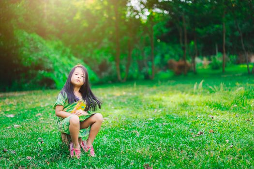 Portrait of happy asian little girl in dress sitting  in the park
