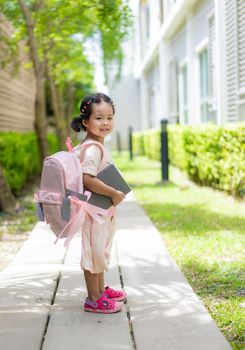 little girl with book and backpack walking in the park ready back to school