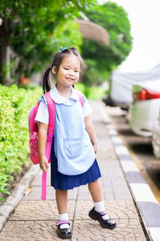 Portrait of happy little girl in Thai school uniform with backpack standing footpath, ready back to school