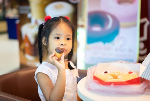 Little asian girl sitting on the chair with holding and eating donuts