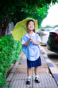 little girl in Thai school uniform with yellow umbrella in raining day