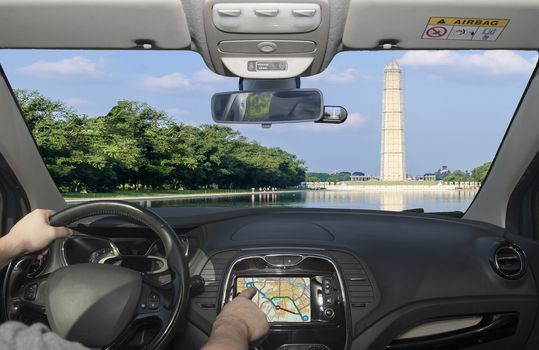 Driving a car while using the touch screen of a GPS navigation system towards the iconic Washington Monument mirroring in the Reflecting Pool, Washington DC, USA
