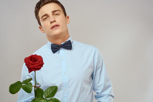 Handsome man with red rose blue shirt bow tie light background cropped view. High quality photo
