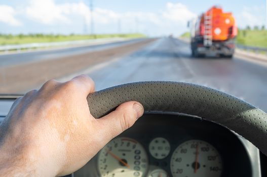 view of the driver hand on the steering wheel of a car that makes a careful overtaking of a fuel tanker, a truck with a fuel tank, with a dangerous flammable cargo