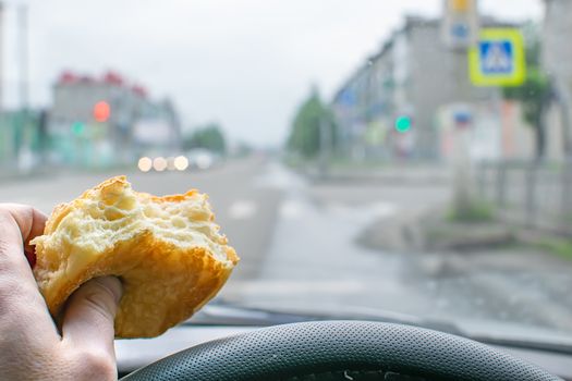 pie, bun, food in the hand of a driver at the wheel of a car who eats while driving on the road near a pedestrian crossing