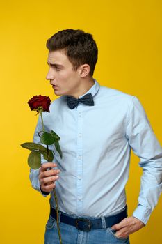 Elegant man in a suit with a red rose in his hands on a yellow background, cropped view. High quality photo