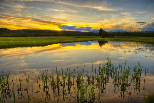 Beautiful vivid sunset at Yellowstone National Park. Mountains and sky is reflecting in a lake. Wyoming, USA