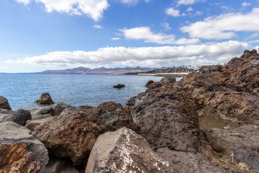 Big lava rocks on the coastline of Puerto del Carmen at Canary island Lanzarote, Spain. The sky is blue with white clouds