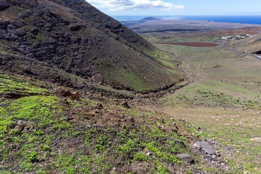 Panoramic view at landscape in the south of canary island Lanzarote nearby Playa Blanca with lava rocks and mountain in the foreground and the atlantic ocean in the background.  The sky is blue with white clouds