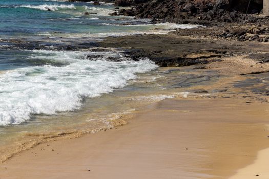 View at the beach and coastline in Morro Jable on canary island Fuerteventura with rough sea, water waves, sand and lava rocks