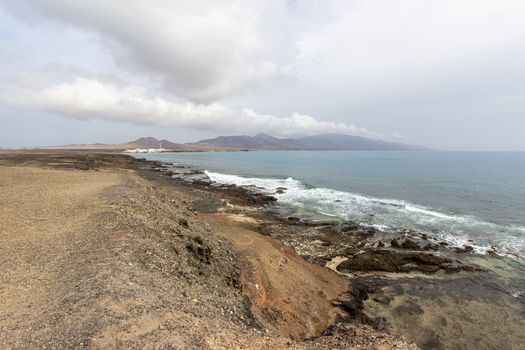 Panoramic view at the coastline in the natural park of Jandia (Parque Natural De Jandina) on canary island Fuerteventura, Spain with gravel, lava rocks and rough sea with waves and mountain range