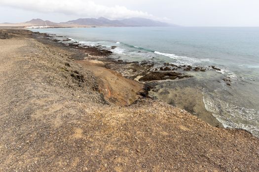 Panoramic view at the coastline in the natural park of Jandia (Parque Natural De Jandina) on canary island Fuerteventura, Spain with gravel, lava rocks and rough sea with waves and mountain 