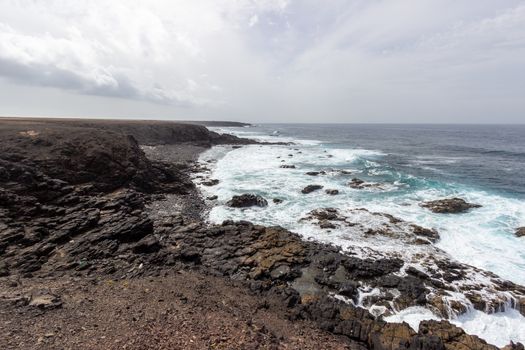 Scenic view at the coastline in the natural park of Jandia (Parque Natural De Jandina) on canary island Fuerteventura, Spain with gravel, lava rocks and rough sea with waves