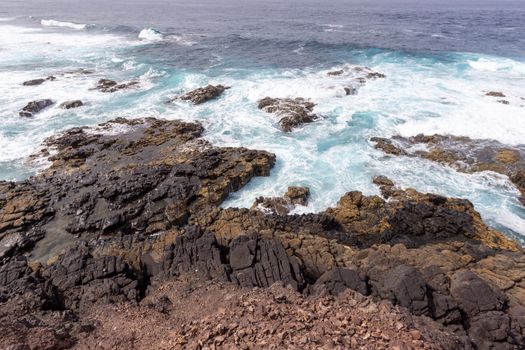 Scenic view at the coastline in the natural park of Jandia (Parque Natural De Jandina) on canary island Fuerteventura, Spain with lava rocks and rough sea with waves