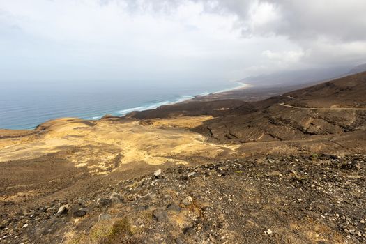 Panoramic view at the coastline in the natural park of Jandia (Parque Natural De Jandina) on canary island Fuerteventura, Spain with gravel, lava rocks and rough sea with waves and mountain range 