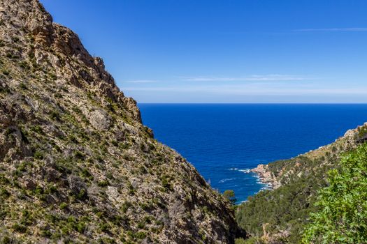 Scenic view in summer at the north coast of Mallorca with mountain in foreground, blue water and blue sky in background 