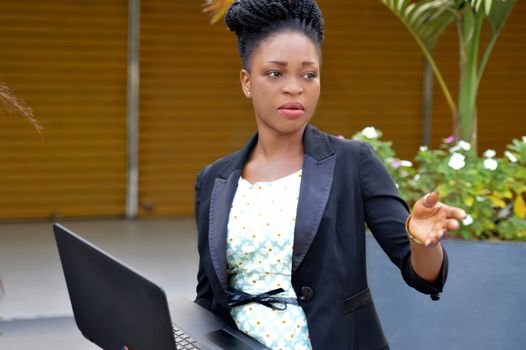beautiful African woman holding a laptop, motions to someone beside her.