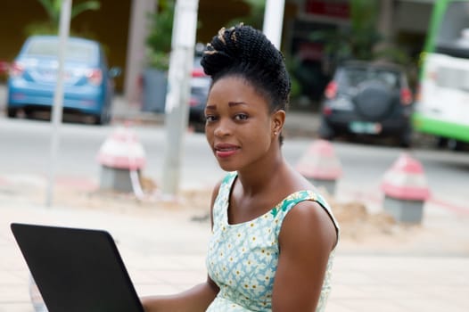 young businesswoman sitting outside working on laptop resting on her lap.