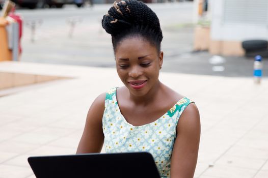 young smiling business woman sitting outside is focused on her laptop.