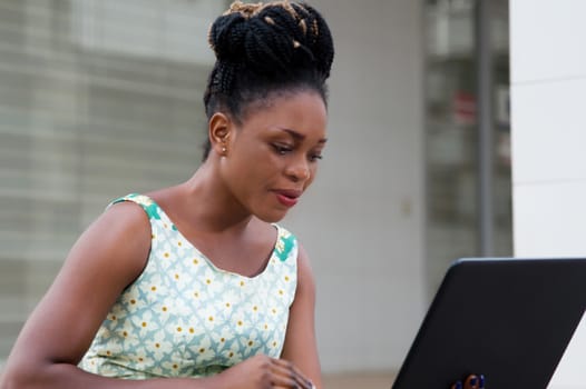 young businesswoman sitting outside working on laptop resting on her lap.