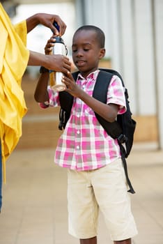 Happy little boy takes his bottle of water in his mother's hand in the morning.