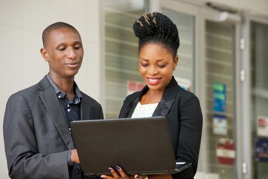 young couple of happy business people standing sharing a laptop in hands