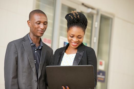 young couple of happy business people standing sharing a laptop in hands