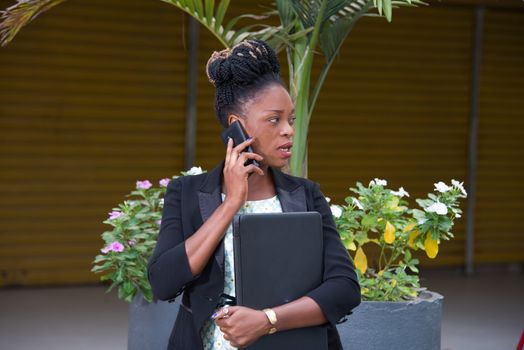 young businesswoman standing calling on the phone and holding a laptop