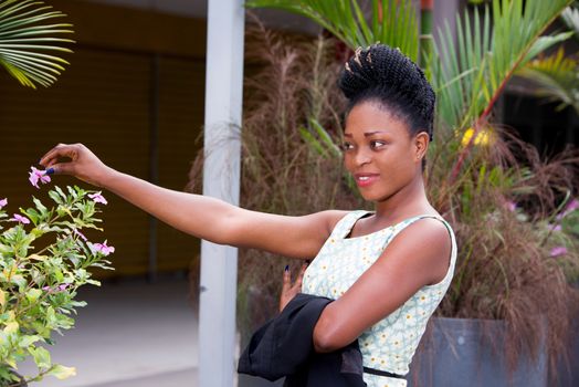 happy young woman pausing alone in front of a flower pot in the street after work