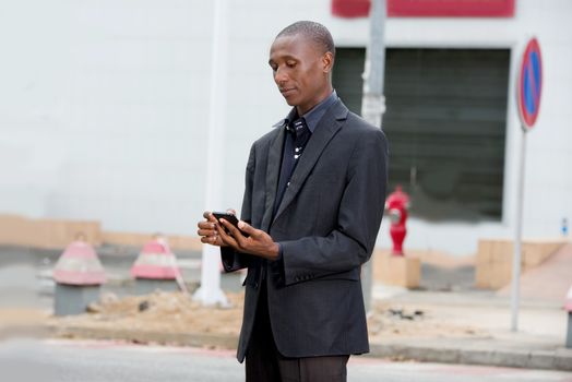 professional businessman in suit standing alone in town and manipulating his mobile phone outdoors
