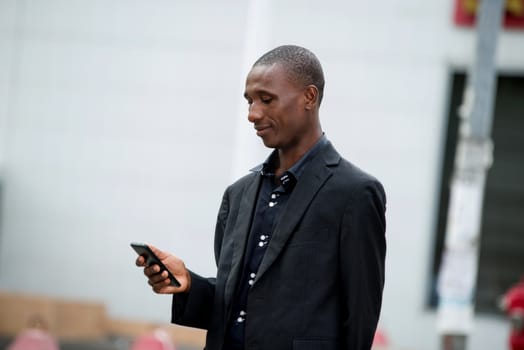 Image of a businessman in a suit standing on the street and checking his mobile phone