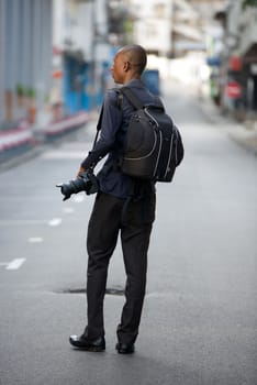 Young man tourist exploring alone while walking with a camera and a backpack and observes the place to take pictures.