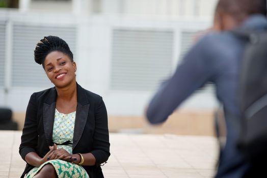 Photographer photographing a cheerful model in a black suit sitting outdoors