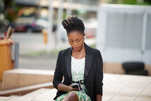 attractive young woman sitting alone outdoors relaxes listening to music on her mobile phone
