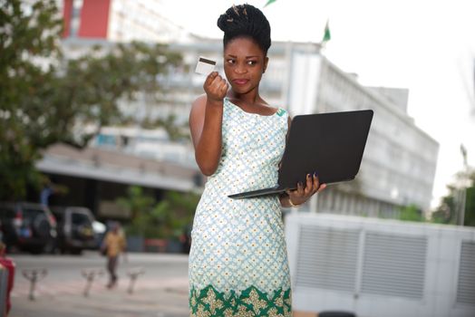 businesswoman standing in the street doing shopping on the laptop with a credit card