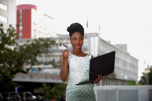businesswoman standing in the street doing shopping on the laptop with a credit card