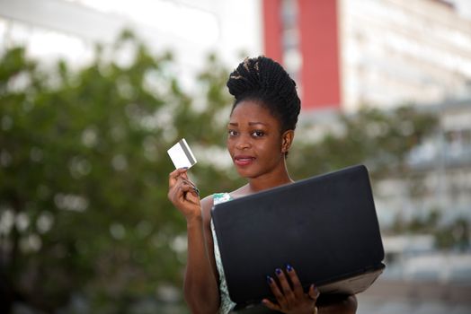 Smiling and confident businesswoman doing online shopping through a laptop and a credit card standing in the street