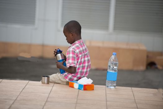 little boy sitting on a terrace with a bottle of water in hand and back him another bottle of mineral water and tissues handkerchief.