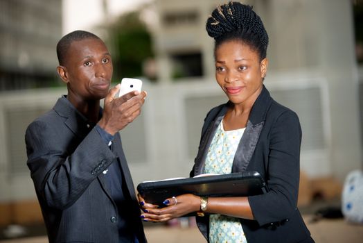 young smiling businesswoman is holding a laptop and beside her, her thoughtful colleague is holding a cellphone.