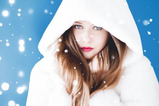 Happy Christmas and winter holiday portrait of young woman in white hooded fur coat, snow on blue background, fashion and lifestyle campaign