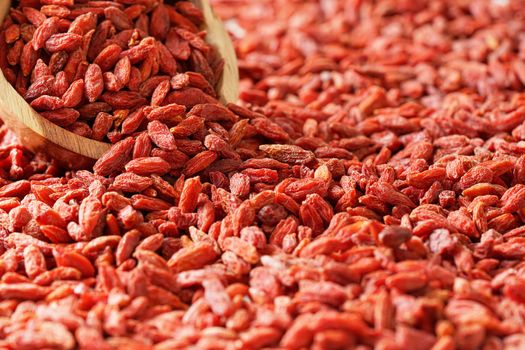 Dry goji berries in small wooden bowl, scattered on desk below.