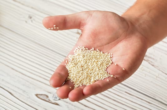 White sesame seeds in man hand, closeup detail, blurred boards table under.