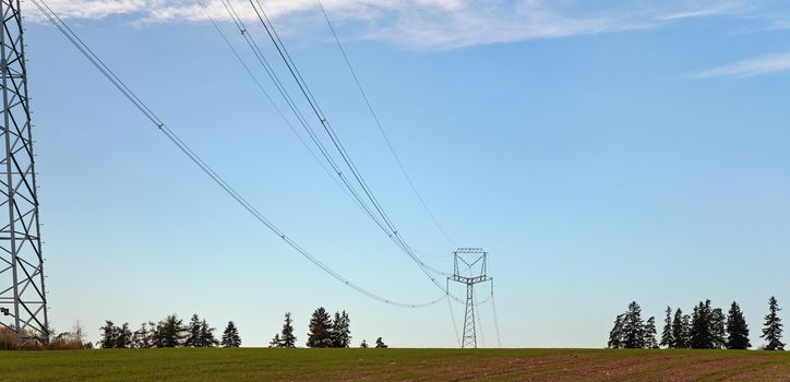 Tall steel power cable pylons supporting electricity cables over flat ground, some trees in distance.