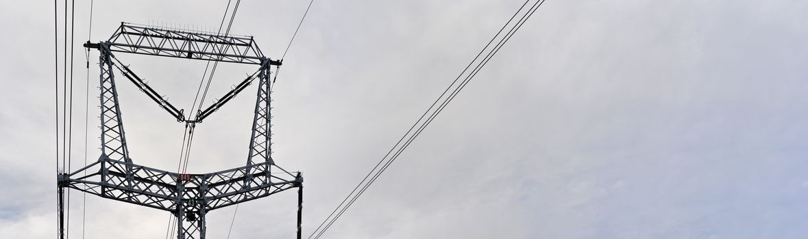 Steel power pylon construction with high voltage cables against cloudy sky. Wide banner for electric energy industry space for text on right side.