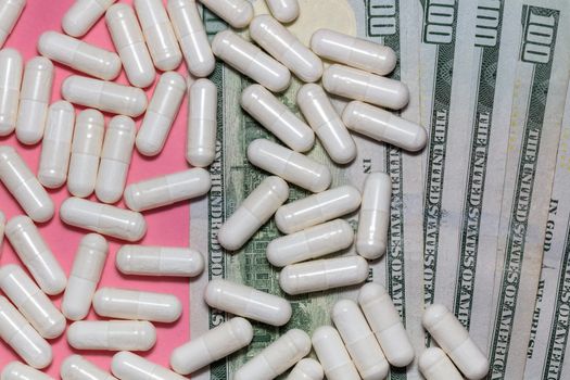 Top close up shot of white pills scattered on top of a few hundreed dollar bills. Pink background. Healthcare, medical, pharmaceutical business, commerce, shopping concepts. New normal concept.