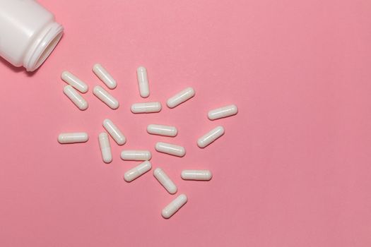 Top view of scattered prescription white pills and a container on pink background with copy space. Healthcare, medical and pharmaceutical concept.