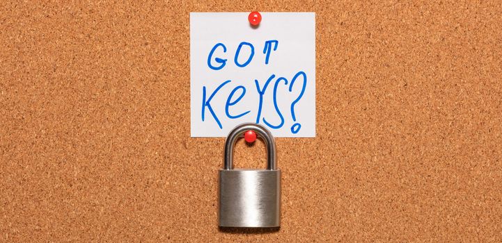 Closed padlock hanging on an empty notice board in business office. White sticky note above the padlock says Got Keys?. Safety, security reminder, business closure concepts. Close up shot. Banner size