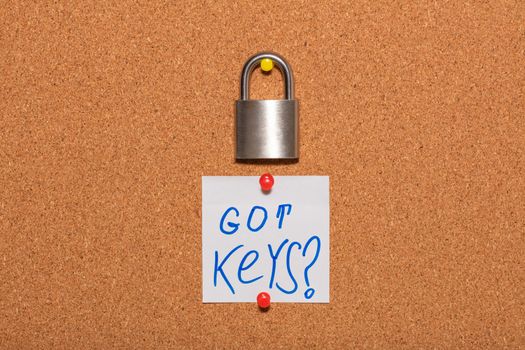 Closed padlock hanging on an empty corkwood notice board in business office. White sticky note below the padlock says Got Keys?. Safety and security reminder, business closure concepts. Close up shot