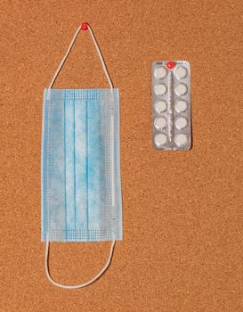 Medical mask and white pills pinned on a corkwood notice board. Healthcare concept.