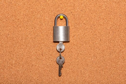 Closed padlock with keys hanging from it on an empty corkwood notice board in business office. Safety and security reminder, business closure, business for sale concepts.